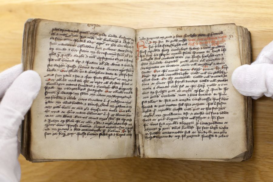 Nærbilde av noen med hansker som holder en gammel bok med gammeldags skrift.