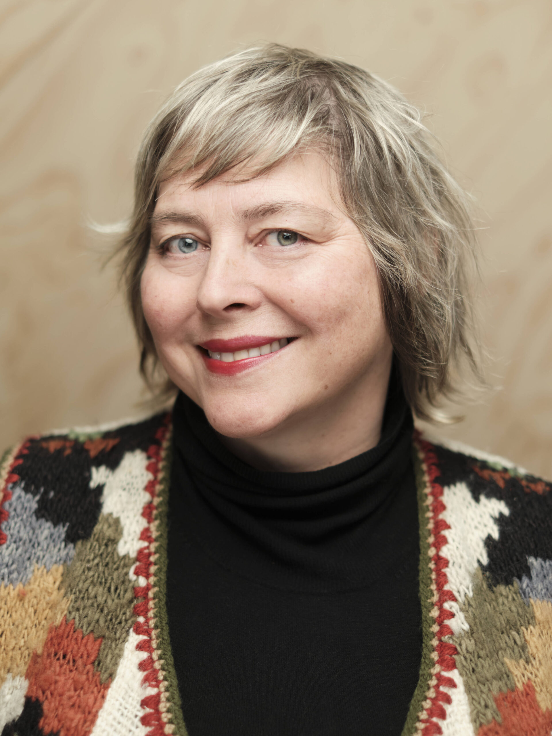 Bilde av Mari Nilsen Neira. Hun smiler til kamera, og har på seg en fargerik cardigan, Hun har kort, blondt hår.
