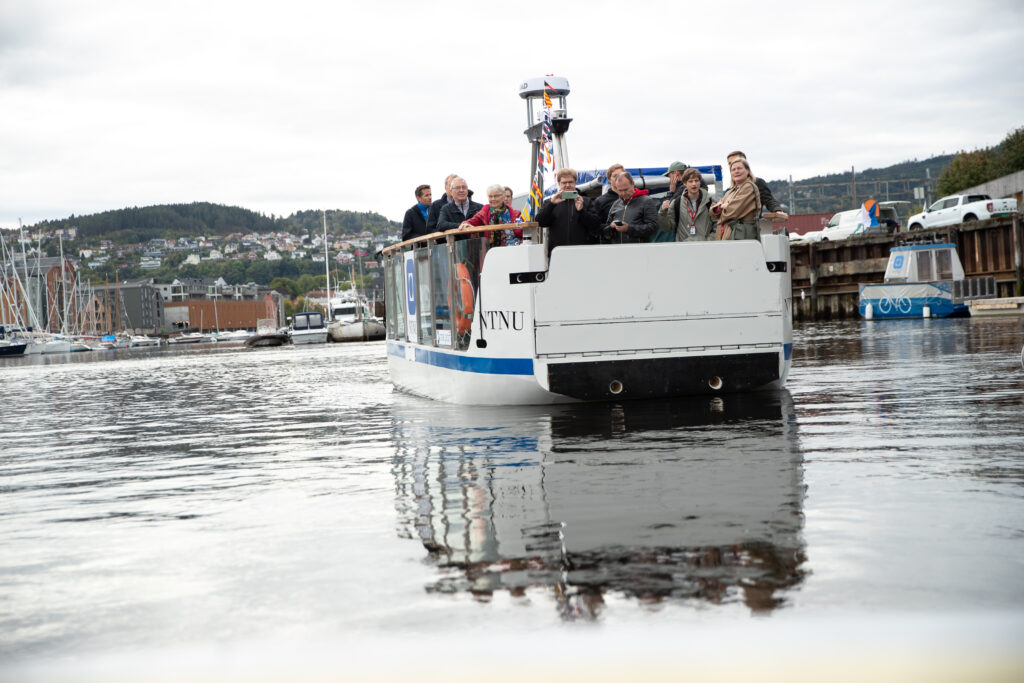 Bilde av en ferge med folk på. vannet er speilblankt.